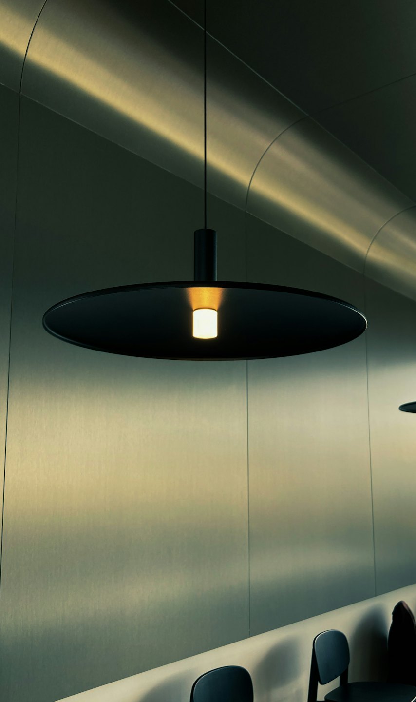 Schwarze Pendelleuchte beleuchtet einen modernen Raum mit metallischen Wänden.