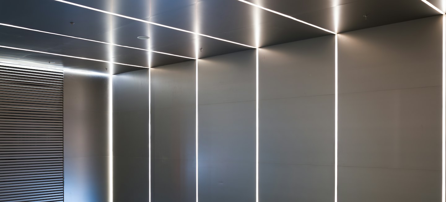 Lineare LED-Leuchten beleuchten graue Paneele in einem minimalistischen Raum.